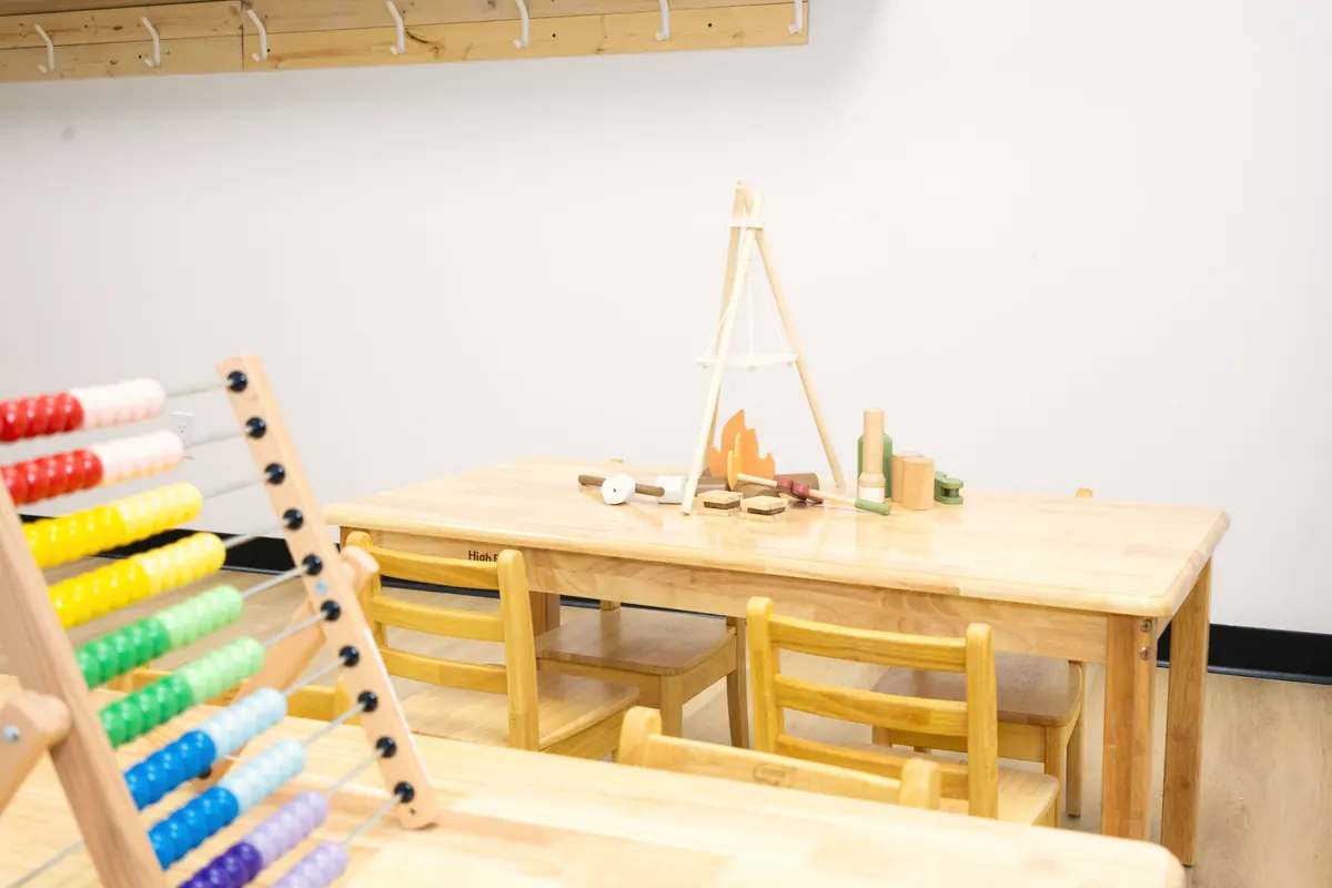 A wooden play set on a low table with a rainbow abacus in front