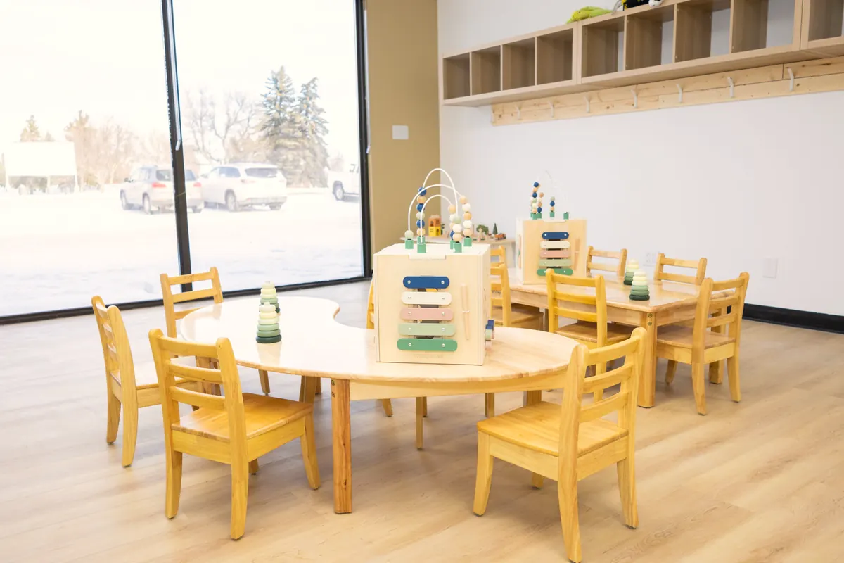 Kidney-shaped child-size table with wooden chairs beside a large window