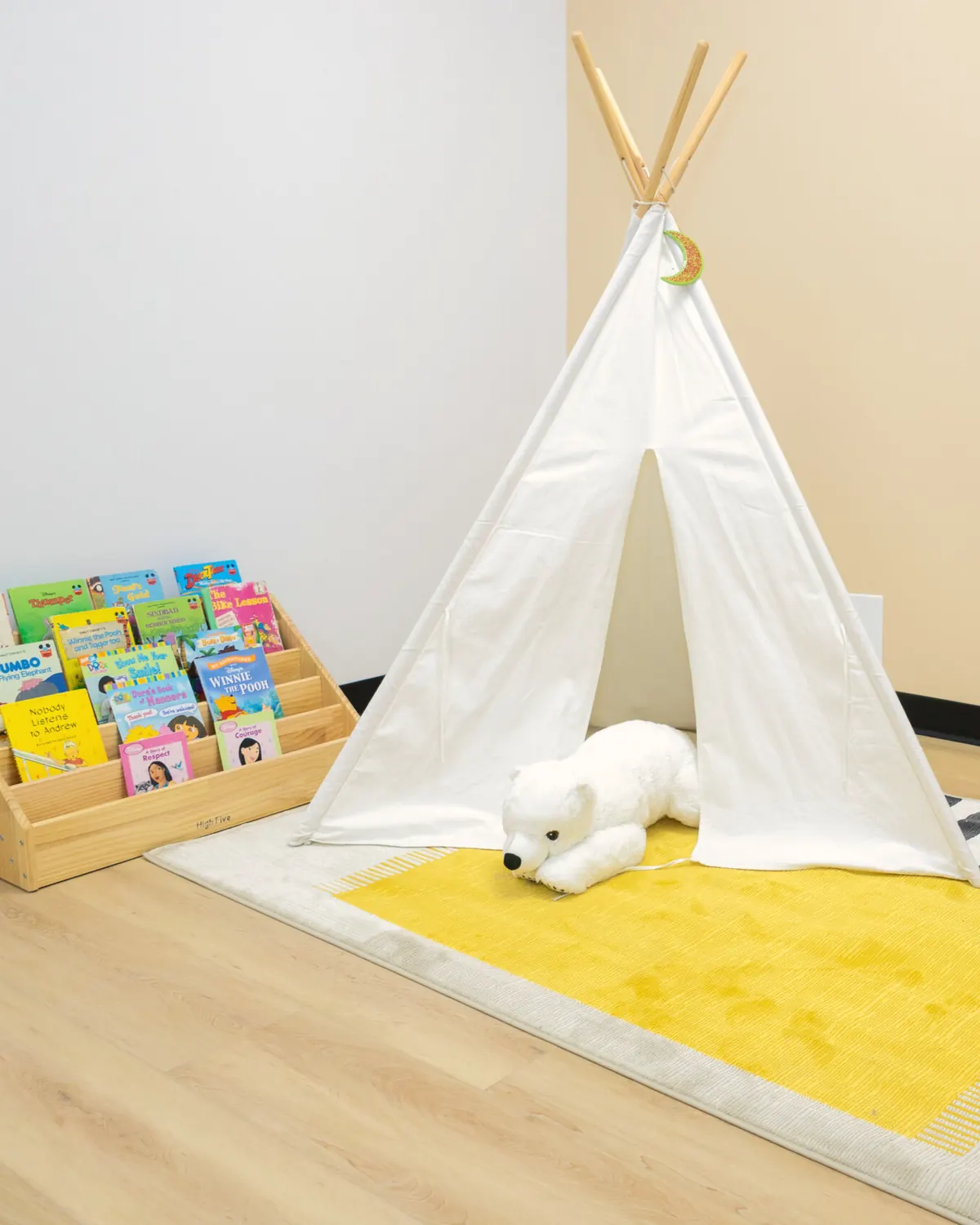 Canvas teepee with a toy polar bear on a yellow rug beside a front-facing book display